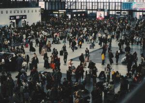 Large crowd of people with luggage at a busy train station during peak hours.