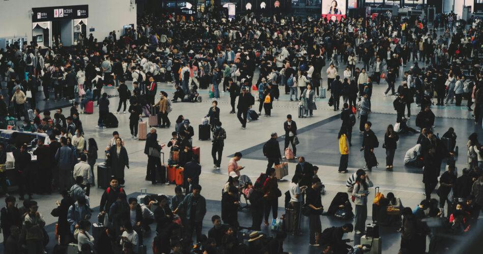 Large crowd of people with luggage at a busy train station during peak hours.