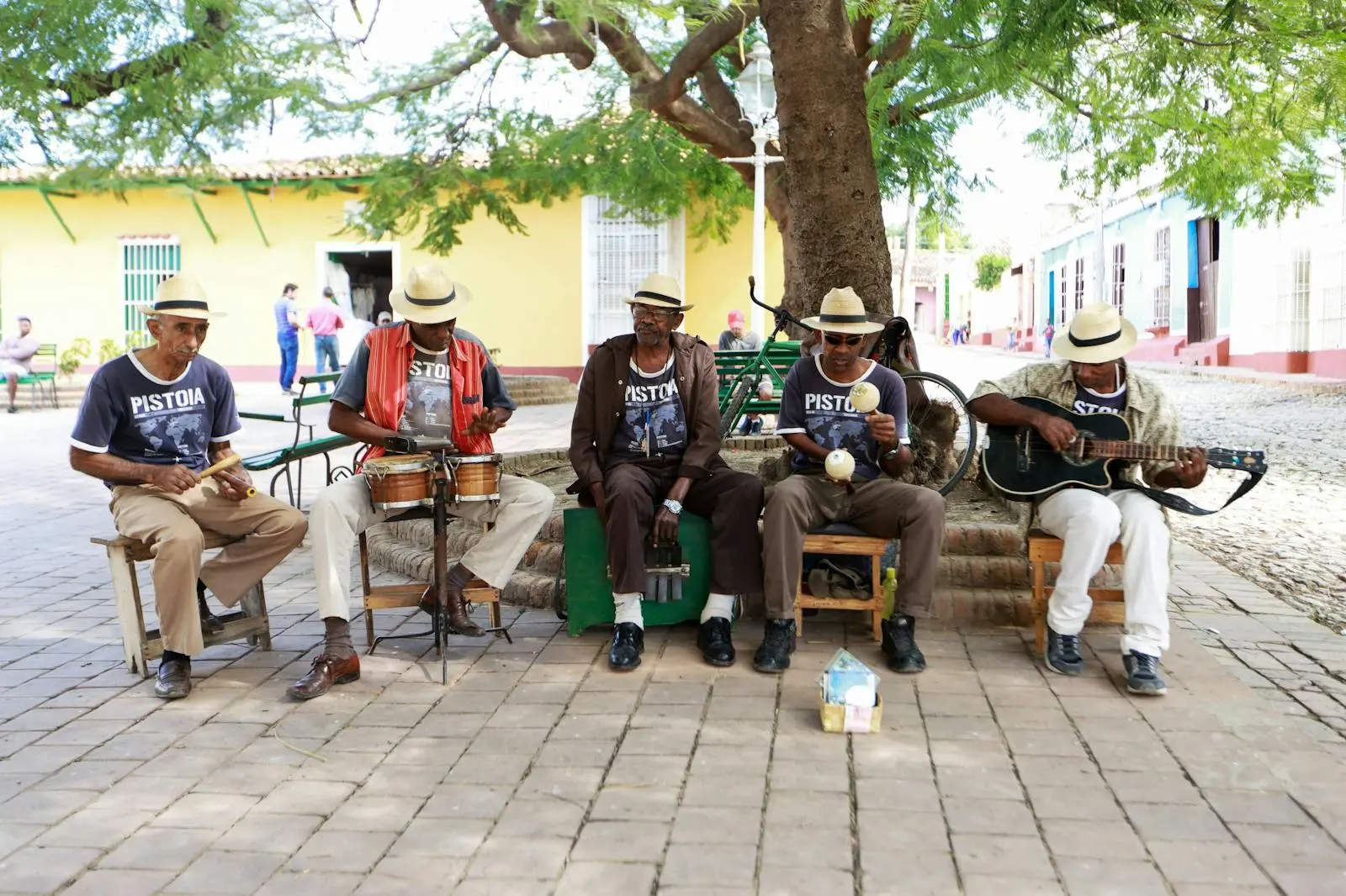 Photo by Mehmet Turgut Kirkgoz Group of musicians playing various instruments under a tree on a vibrant street.